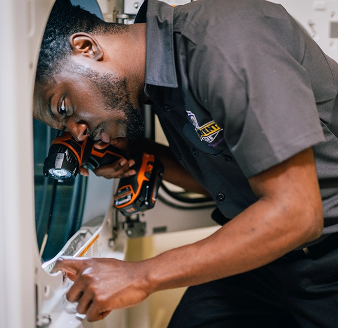 Technician holding flashlight to see the inside of a dryer lint trap.